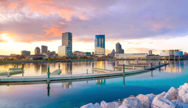 Milwaukee skyline at twilight with city reflection in lake Michigan and harbor pier.