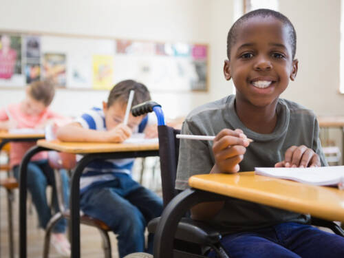 Boy in a wheelchair smiling in a classroom